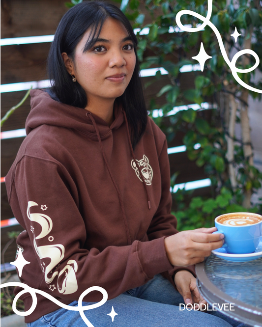 Person wearing a brown hoodie with a logo, holding a blue cup outdoors.