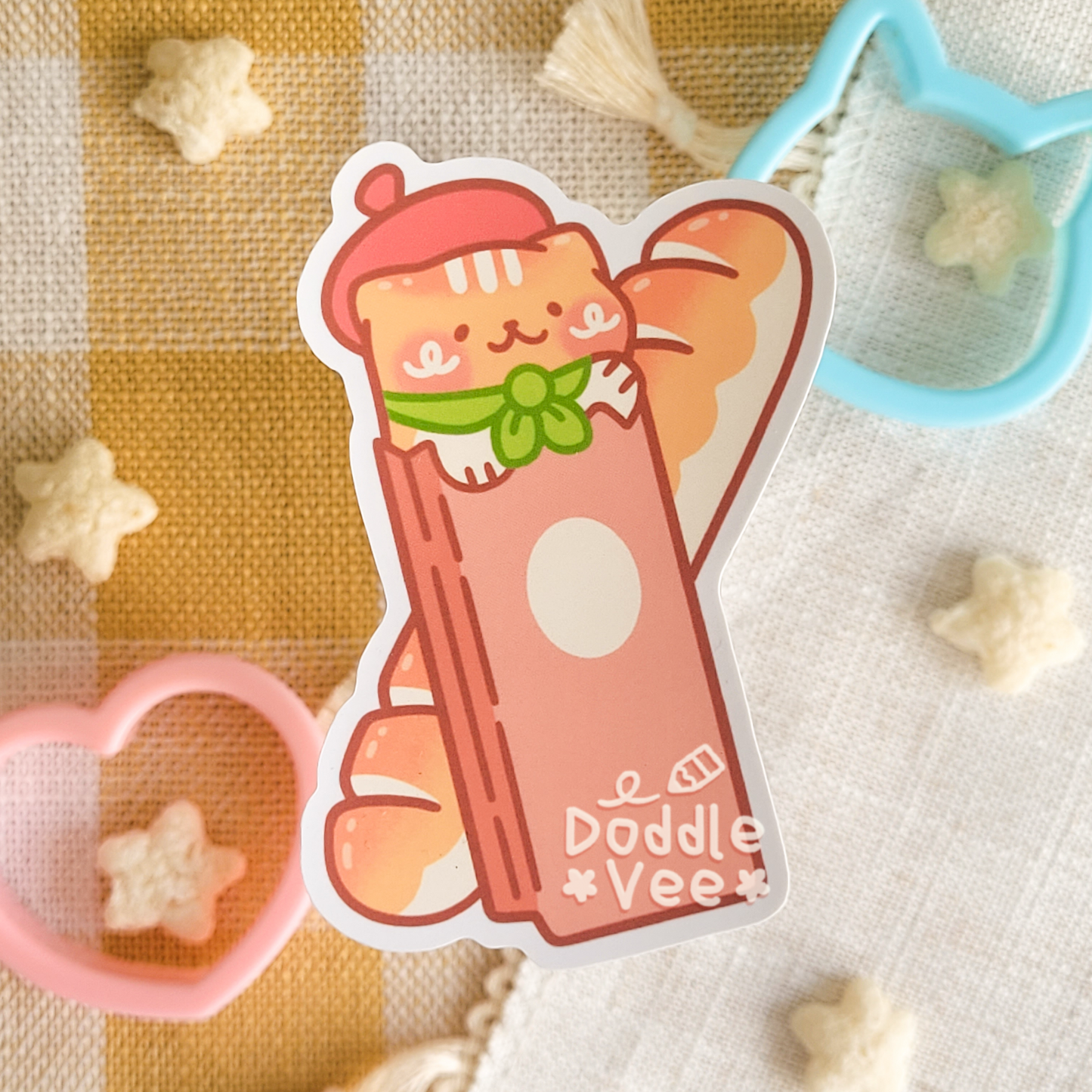 Sticker of cat in bag wearing berat with a baguette behind it