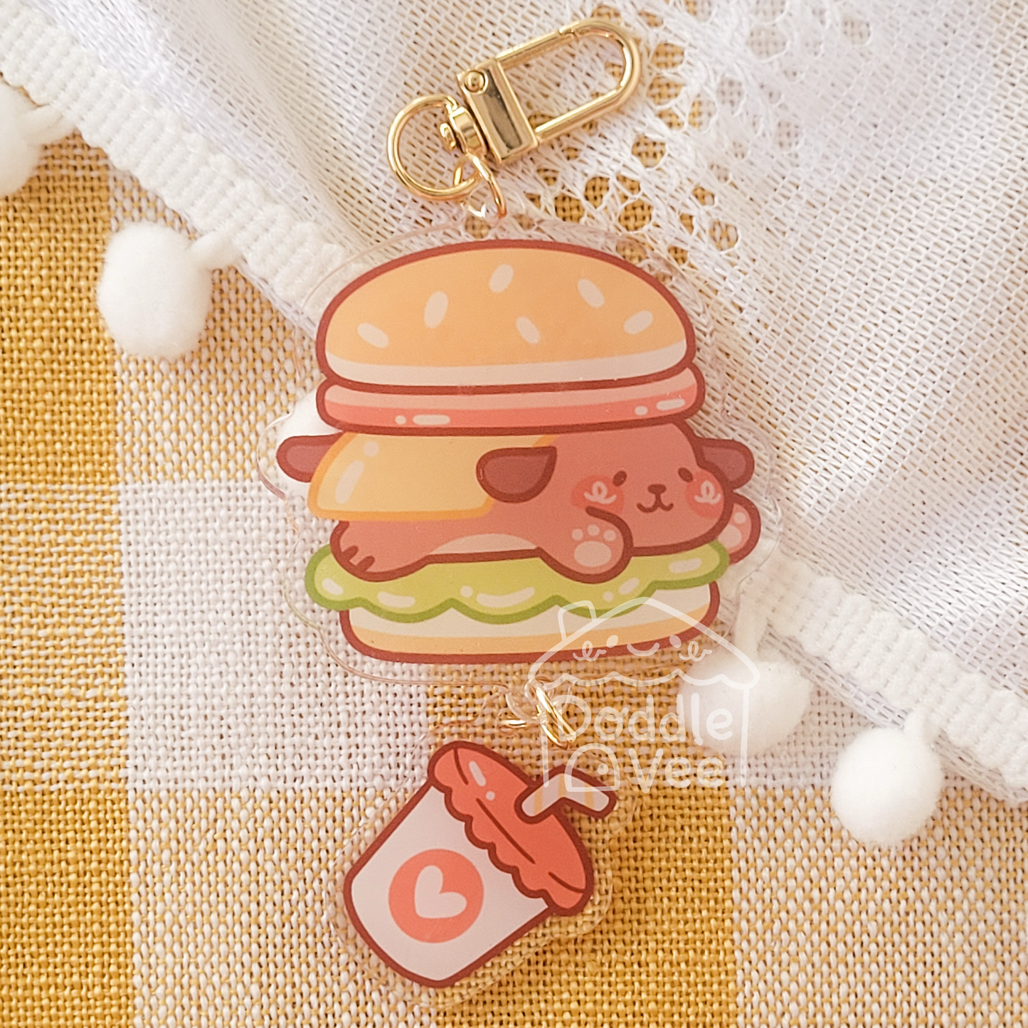 Cute cartoon hamburger keychain with a small bottle charm on a checkered fabric background.