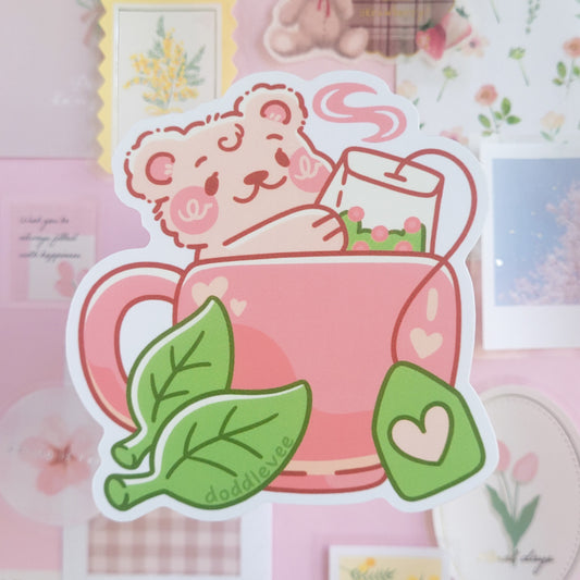 Sticker of a bear holding a teapot with tea leaves on a pink background
