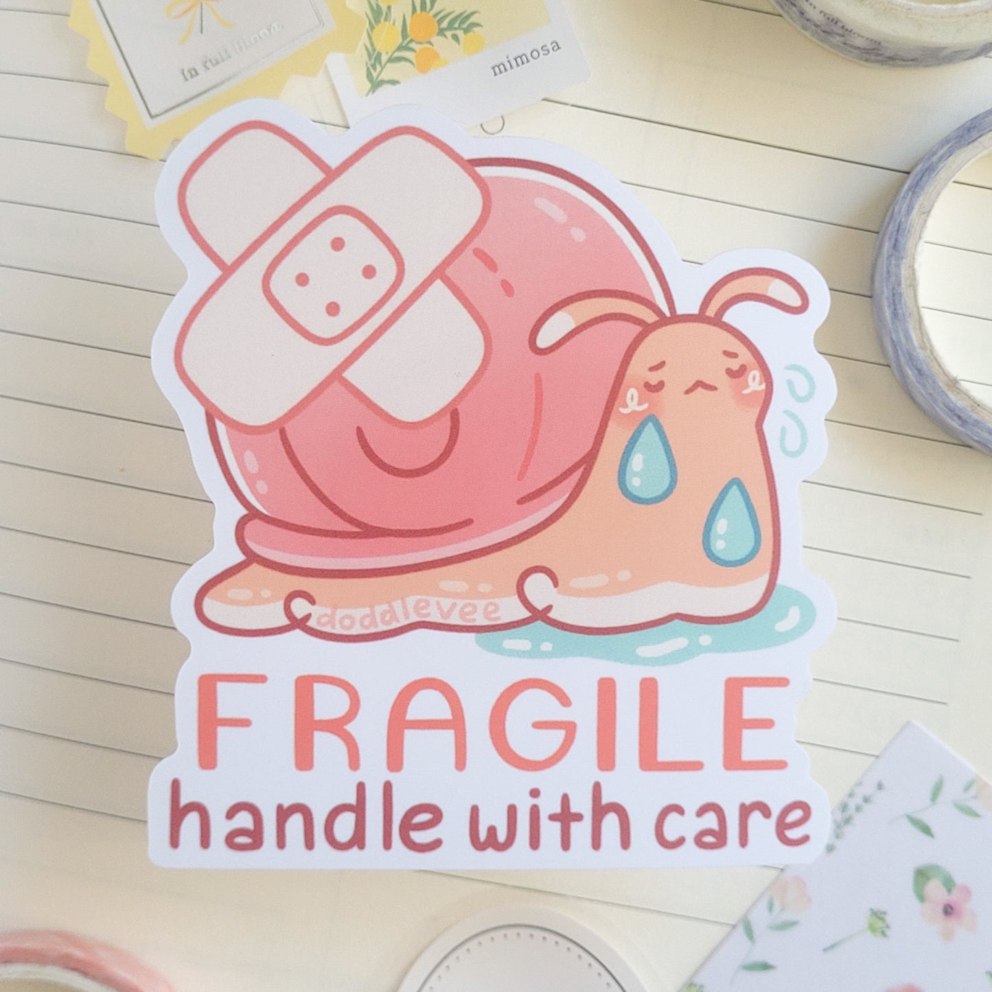Sticker of snail with a band aid on its shell with the words on the sticker saying Fragile Handle with Care.