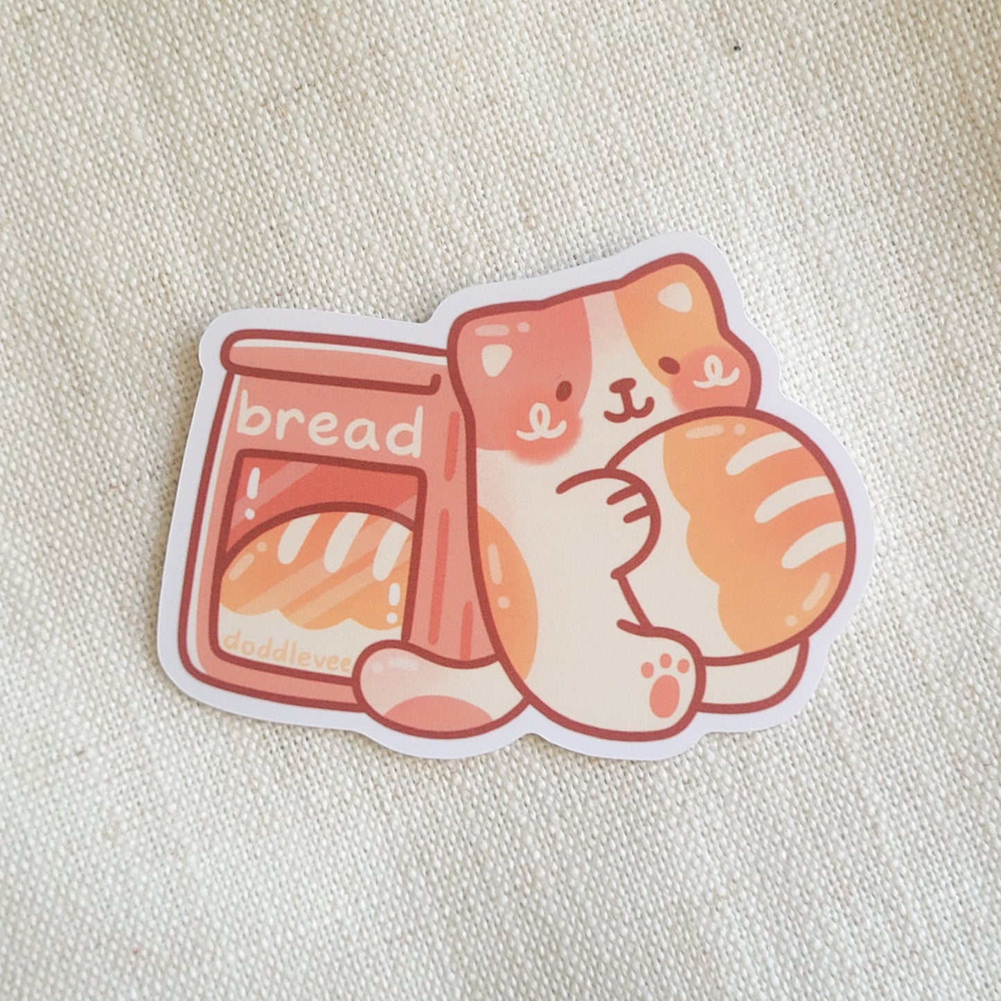 Sticker with calico cat holding bread loaf sitting next to bag with bread inside of it.