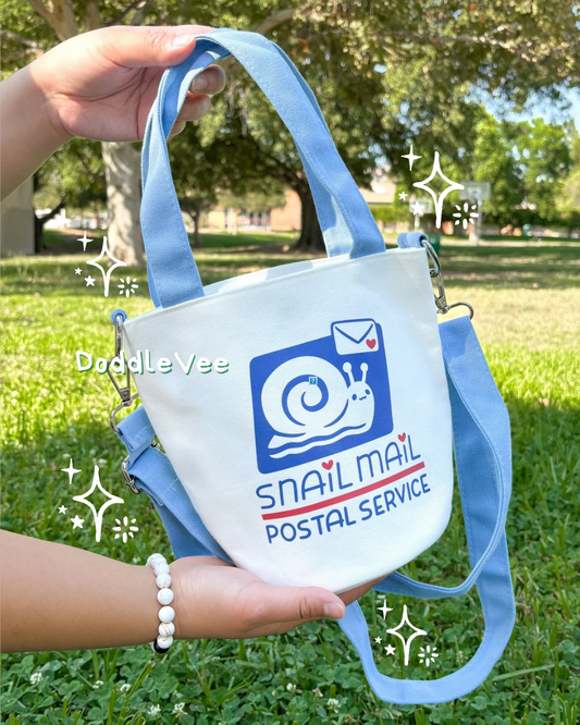 Hand holding a small bag with a snail mail logo against a grassy outdoor background