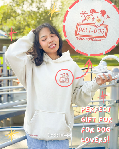 Person wearing a white hoodie with a brand logo, standing outdoors with a 'Deli-Dog' sign in the background.