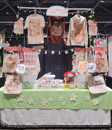 Display of clothing and bags with a green tablecloth and floral decorations at an event.