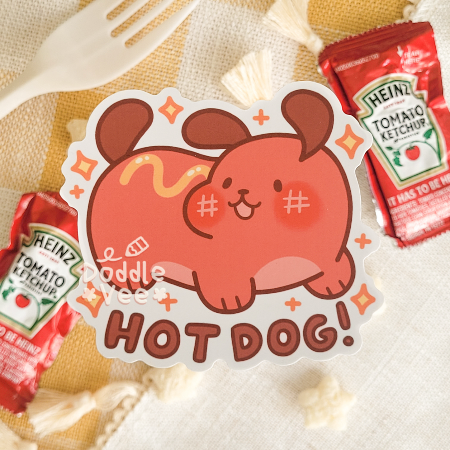 Cartoon dog sticker with 'Hot Dog!' text on a background with Heinz ketchup packets.