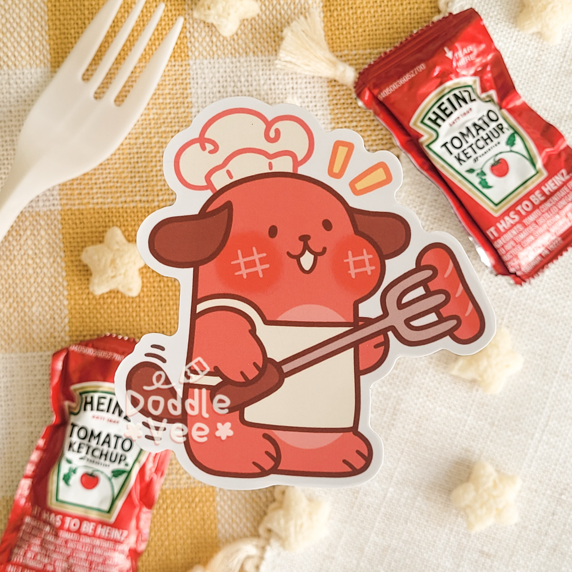 Sticker of a cartoon dog holding a Heinz tomato ketchup packet on a checkered cloth with a fork and more ketchup packets.