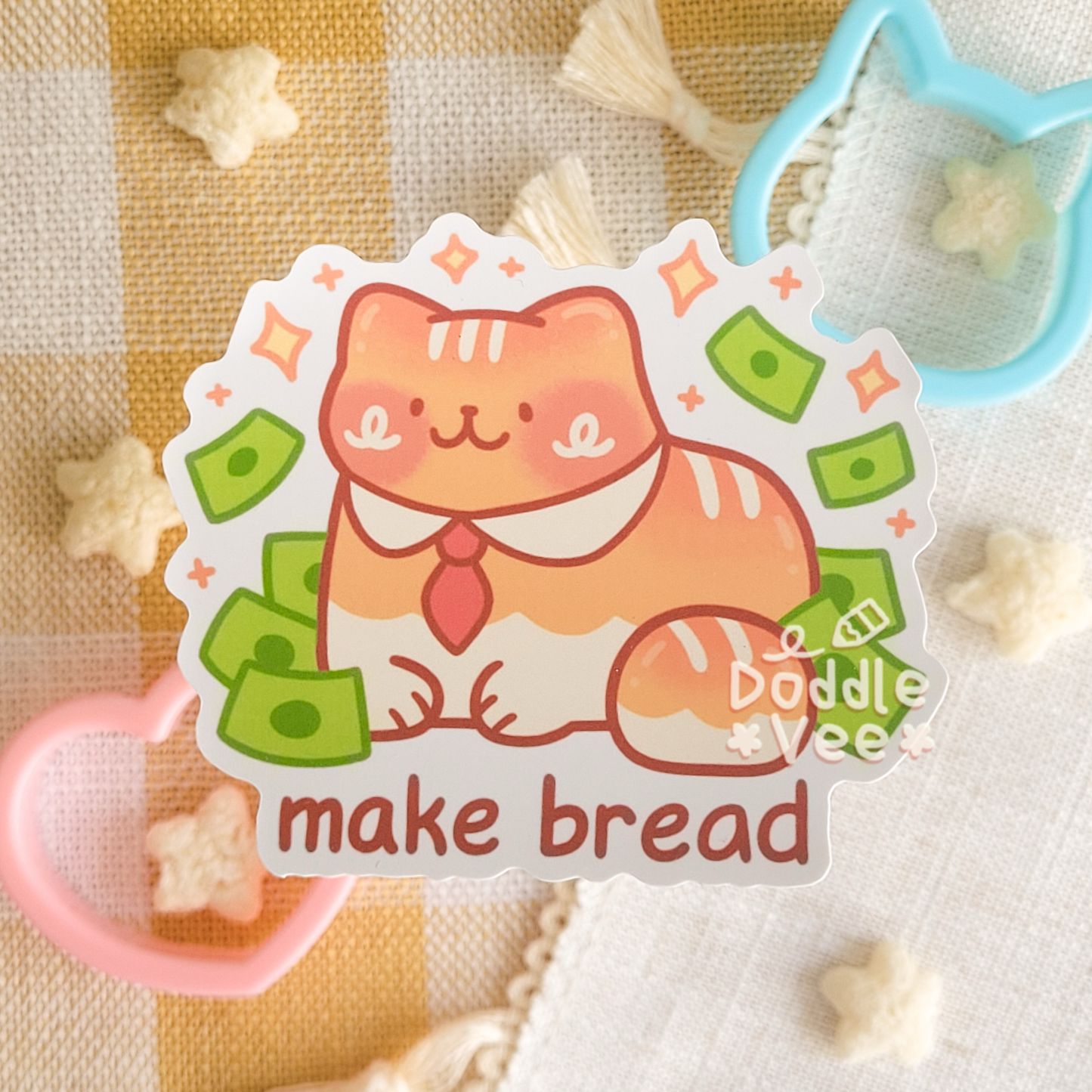 Sticker of little loaf or cat sitting down with dollar bills around it. The words make bread appear on the bottom.