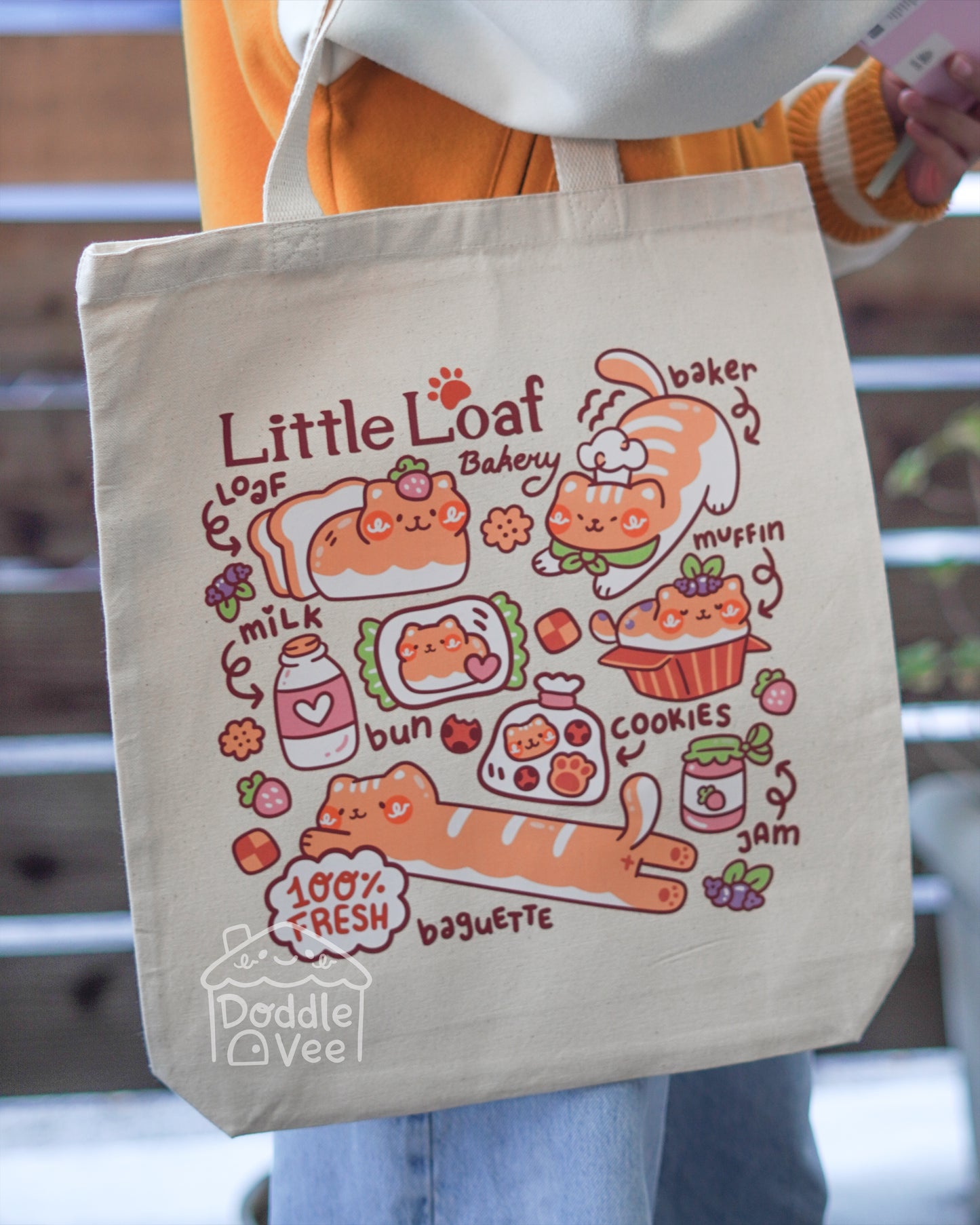 Tote bag with cartoon bakery design and 'Little Loaf' text, held by a person.