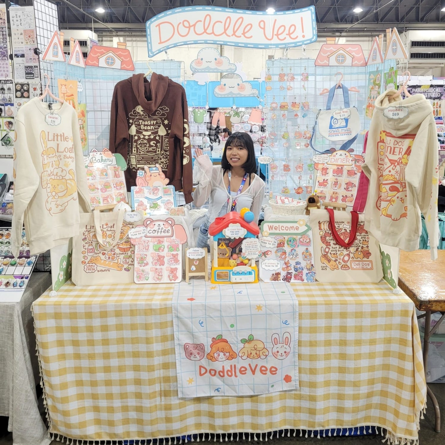 Person standing behind a table with various items at a Doddle Vee booth.
