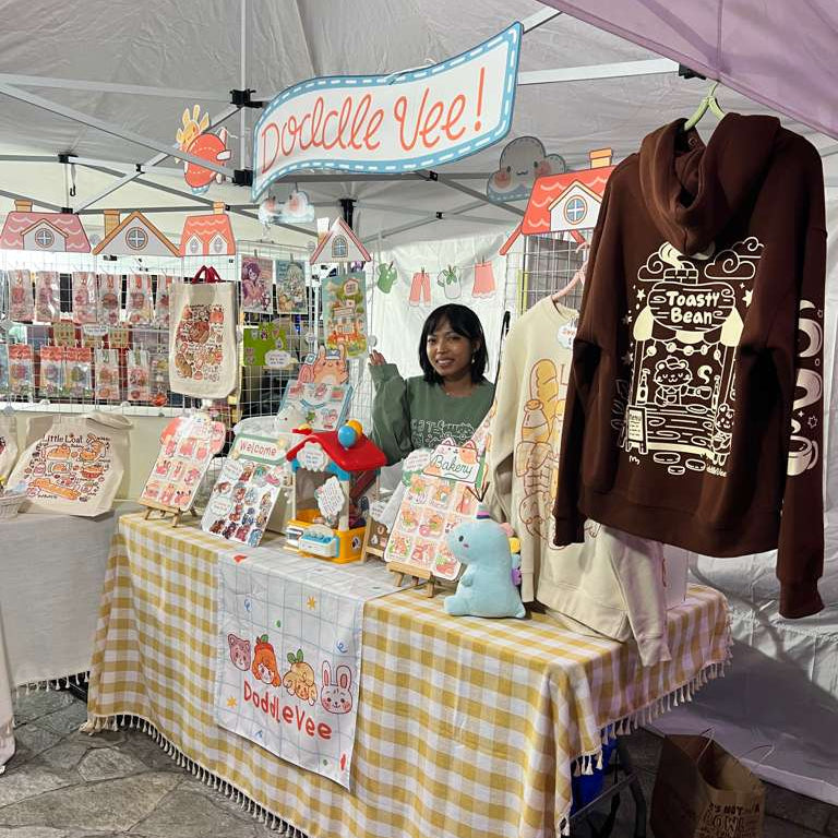 Stall with 'Doddle Vee' branding, featuring a woman behind a table with merchandise.